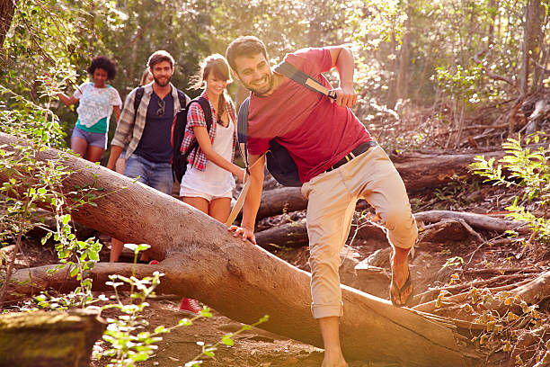 istock Group Of Friends Jumping Over Tree Trunk On Countryside Walk 473422218