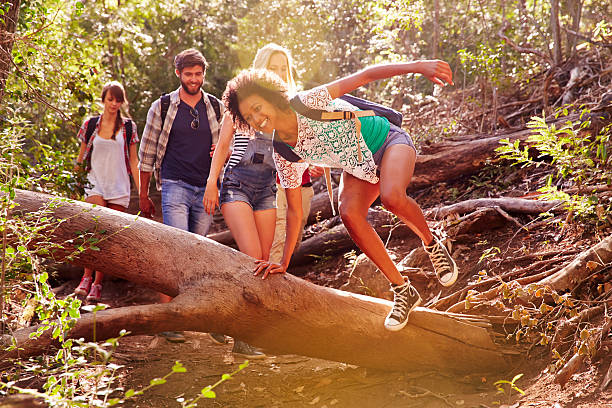 istock Group Of Friends Jumping Over Tree Trunk On Countryside Walk 473423306
