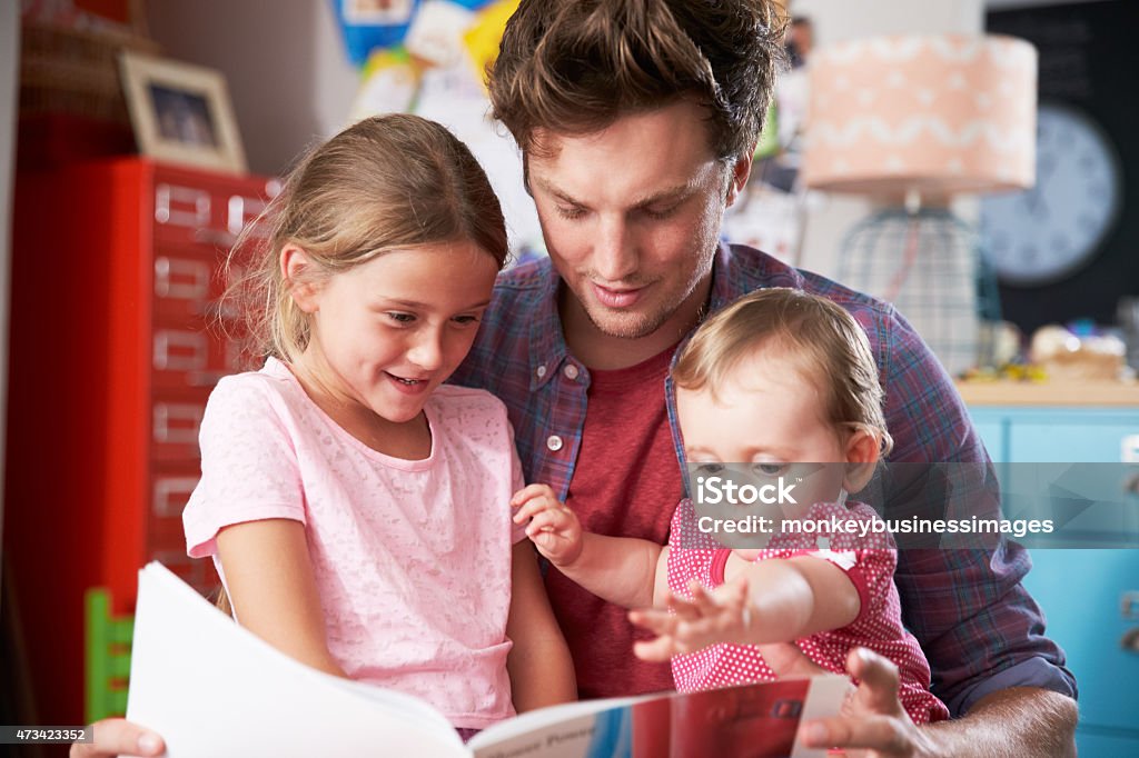 Father Reading Book With Daughters In Bedroom 20-29 Years Stock Photo