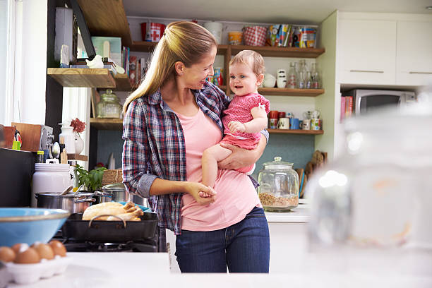 istock Mother Cooking Meal Whilst Holding Daughter In Kitchen 473423524