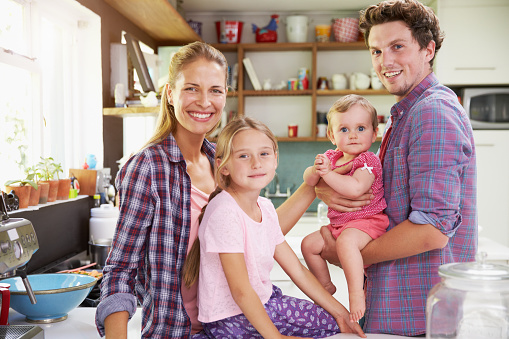 Portrait Of Family Cooking Meal In Kitchen Together. Smiling To Camera