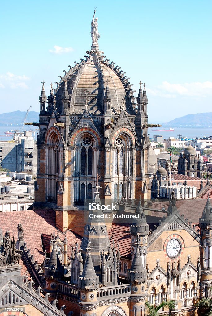 Vertical shot of statue of 'PROGRESS' atop Chatrapati Shivaji Terminus, Mumbai Vertical shot of statue of 'PROGRESS' atop Chatrapati Shivaji Terminus, Mumbai showing its facade and impressive gothic architecture. In the background Mumbai sea-front and surrounding hills can be seen. Copy space. 2015 Stock Photo
