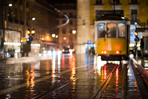 Defocused image of the Lisbon tram at night with reflections after a rainfall.  Focus is on the cobblestone in the foreground.
