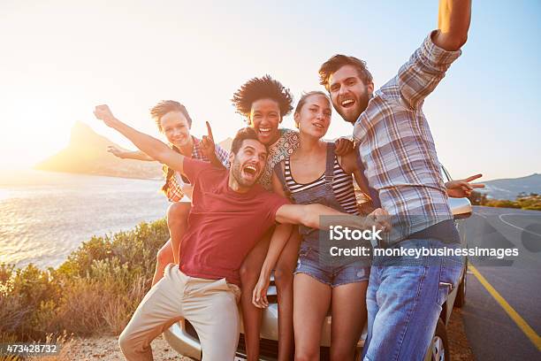 Friends Standing By A Car Next To A Coastal Road At Sunset Stock Photo - Download Image Now