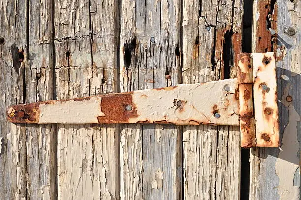 Close up of an old door with cracked paint and rusty hinge.