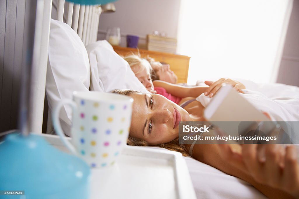 Family In Bed As Mother Reaches To Check Mobile Phone 20-29 Years Stock Photo