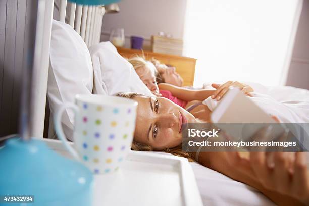 Family In Bed As Mother Reaches To Check Mobile Phone Stock Photo - Download Image Now