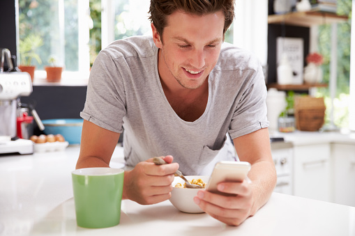 Man Eating Breakfast Whilst Checking Mobile Phone