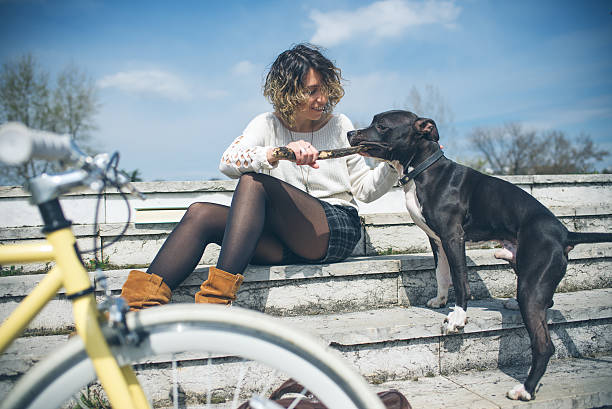 istock Beautiful young woman with bicycle playing with a dog 473435988