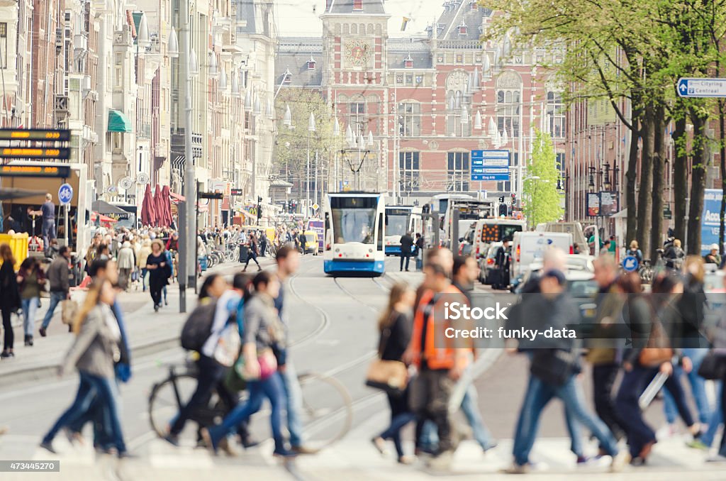 Damrak and central station Amsterdam city center The famous Damrak with the central station in the background. Tourists and locals are walking on crosswalk, a tram is approaching. Selective focus with copy space above. Amsterdam Stock Photo