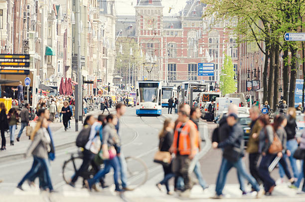 The famous Damrak with the central station in the background. Tourists and locals are walking on crosswalk, a tram is approaching. Selective focus with copy space above.
