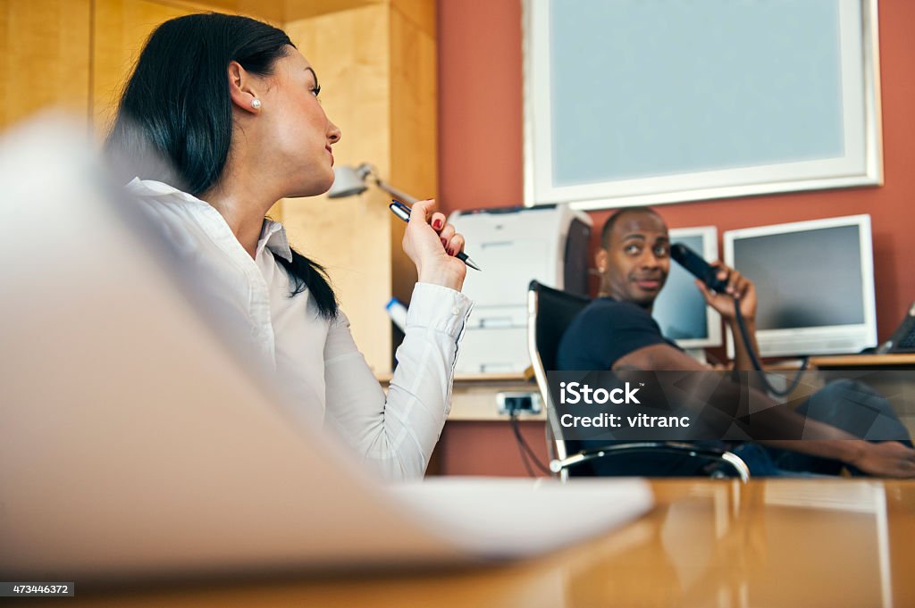 Businesswoman working on laptop at office Businesswoman working on laptop with male partner sitting in background at office Administrator Stock Photo