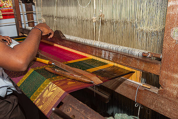 Kanchipuram, Tamil Nadu, India - Weaving The Famous Brightly Coloured Kanchipuram Silk Sari On A Handloom. Kanchipuram, India - January 29, 2015: A weaver on a hand-loom, weaving the famous, much sought after, Indian Conjeevaram or Kanchipuram silk sari in the town of Kanchipuram in Tamil Nadu, South India.  Only about about 15 inches can be woven in a whole day; it takes between 15 to 20 days to weave a whole Sari. Each Sari is unique and the design is hardly ever repeated.  The gold you see in the Sari is real gold, woven into the sari as gold thread.  This is a centuries old craft, that flourishes in this one town in the whole of India.  Kanchipuram saris are a must at South Indian Tamil weddings. Photo shot in the horizontal format.  Focus on the bottom section of the Sari, referred to as the 'Border'. weaverbird photos stock pictures, royalty-free photos & images
