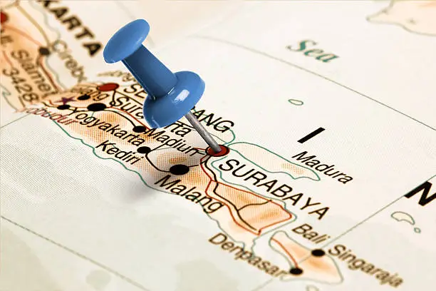 Series: Travel the world and visit major cities. Blue thumbtack (push pin) that is stuck in a map, which marks the city of Surabaya, Indonesia. The map is toned in pastel colors. Concept: Planning travel destinations or journey planning. Close-up view. Studio shot. Landscape orientation.