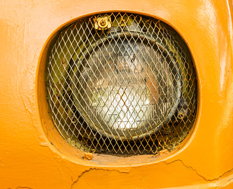 Detail of the front headlight of an old and damaged yellow  vehicle
