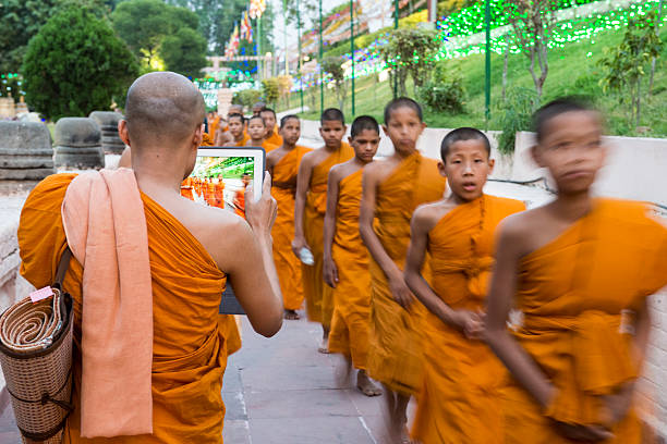Bodhgaya, India - May 4, 2015: A monk takes the photograph of other young monks at the mahabodhi temple premises in his ipad.
