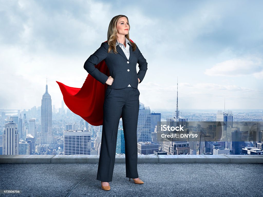 Superhero Businesswoman With Cityscape In The Background A businesswoman wearing a red cape strikes a super hero pose.  Her  hands on her hips and her feet are apart as she stands in front of the New York skyline. Superhero Stock Photo
