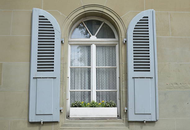 Italian window on the bright white wall facade with open red color classic shutters