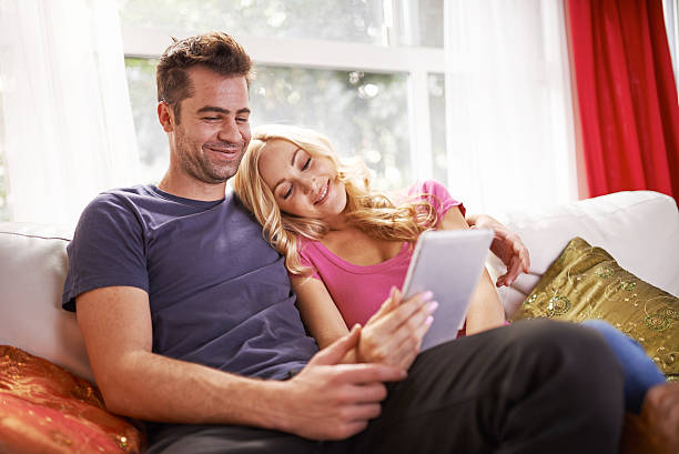 istock couple watching videos or shopping on tablet cuddling 473516228
