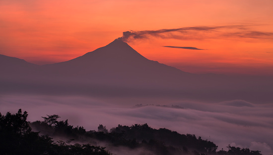 Aerial view of a majestic sunrise over the Merapi volcano in Java. With an altitude of 2930m, the Merapi is a sacred mountain and is located near the cultural city of Yogyakarta in Central Java of Indonesia. The last eruption occurred in 2010 and smokes always rises is from its cone.
