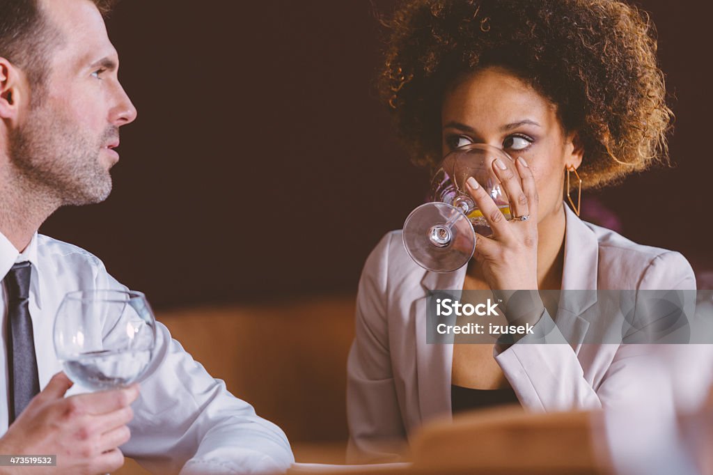 Two business people at lunch in the restaurant An afro american businesswoman and caucasian businessman having lunch or dinner in restaurant, drinking water and talking. Close up of faces. 2015 Stock Photo