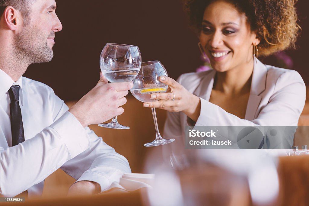 Two happy business people at lunch in the restaurant An afro american businesswoman and caucasian businessman having lunch or dinner in restaurant, sitting at the table, laughing and toasting with glass wine. 2015 Stock Photo