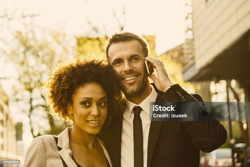 Outdoor portrait of elegant couple, man talking on phone Outdoor portrait of cheerful, elegant couple - afro amercian woman and caucasian man at sunset, man talking on smart phone. Close up of faces. 2015 Stock Photo