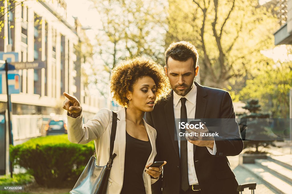 Outdoor portrait of two business people with smart phones Outdoor portrait of caucasian businessman and afro-american businesswoman using a smart phones at sunset. Woman pointing with index finger. African Ethnicity Stock Photo