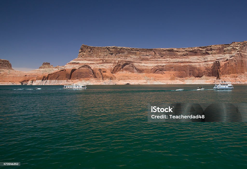 Houseboats on Lake  Powell Two houseboats on Lake Powell motoring beneath a clear deep blue sky and red and orange tarnished rock cliffs. 2015 Stock Photo