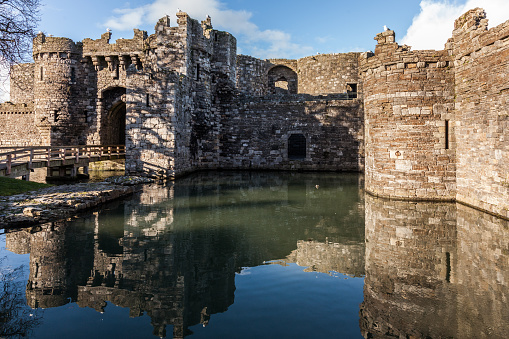 Beaumaris, Wales - February 21, 2015: Castle keep and moat, Beaumaris Castle on the Isle of Anglesey medieval Castle in Britain birds sit on the wall above the gate. A wooden bridge crosses the moat. the castle is reflected in the water