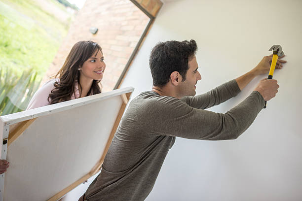 Couple hanging a painting Happy young couple hanging a painting together at home - lifestyle concepts hammer photos stock pictures, royalty-free photos & images