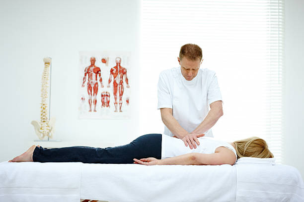 Male osteopath treating back problem of a woman Male osteopath treating back problem of a woman lying on medical room alternative healthcare worker stock pictures, royalty-free photos & images