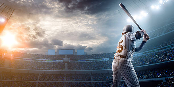 Baseball player in stadium A male baseballs batter makes a dramatic play.  The stadium is blurred behind him. Only the lights of the stadium shine brightly, creating a halo effect around the bulbs. baseball player at bat stock pictures, royalty-free photos & images