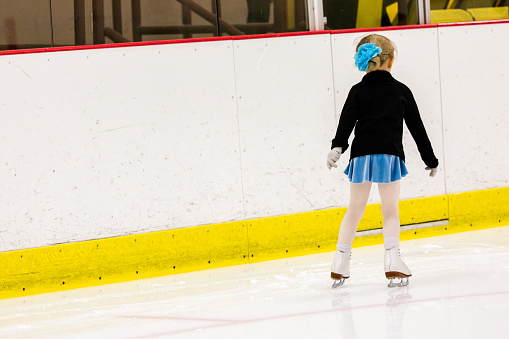 Cute young girl practicing figure skating on indoor ice skating rink.