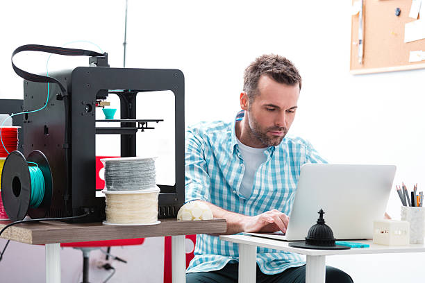 Man in 3D printer office using laptop Man working in a 3d printer office, sitting at the table and using laptop. 3d printing filament photos stock pictures, royalty-free photos & images