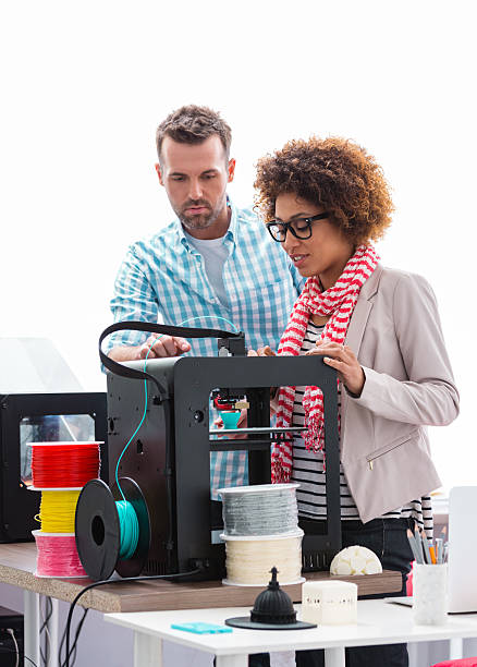 Woman and man in 3D printer office Two business colleagues - afro american woman and caucasian man, working together in a 3d printer office, watching 3d printout. 3d printing photos stock pictures, royalty-free photos & images
