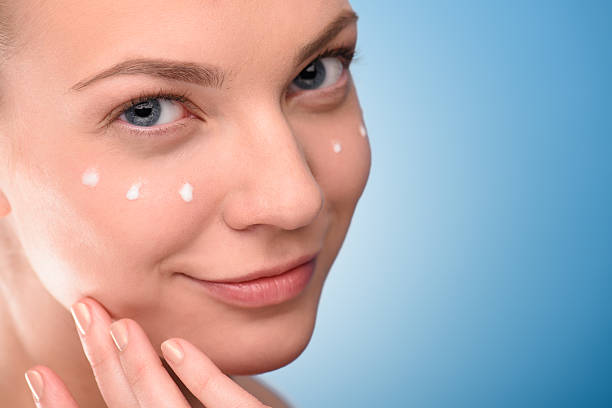 istock Woman applying lifting cream on face, over blue background 473583852