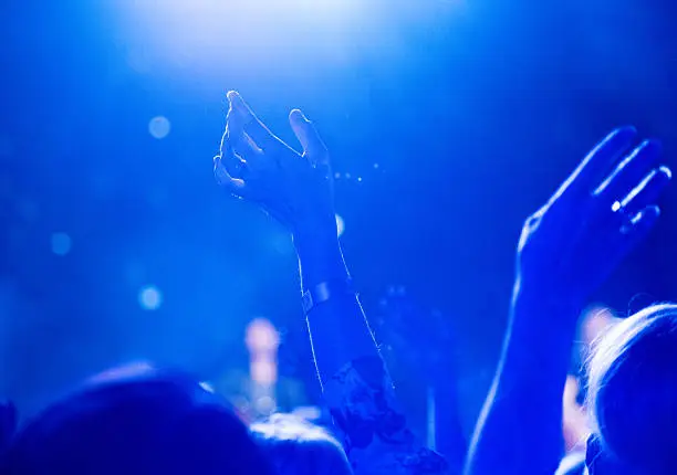 Photo of Hands raise at concert with ambient blue light haze