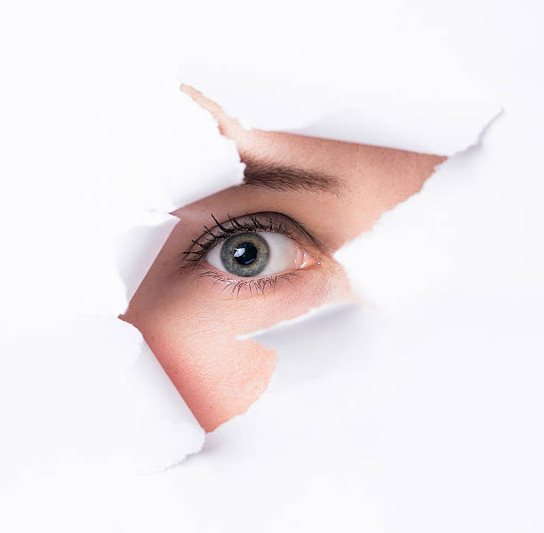 istock Women  eyes through a hole in a paper 473607128