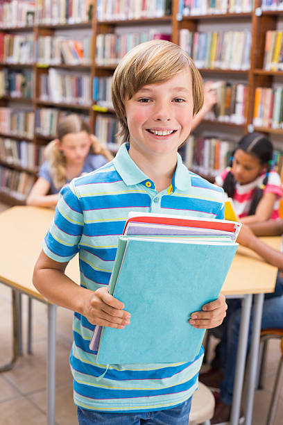 istock Cute pupil smiling at camera in library 473607558