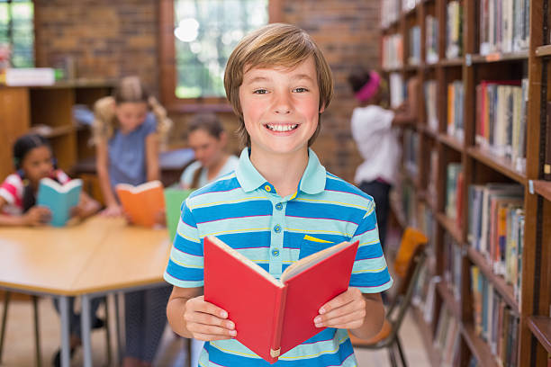 istock Cute pupil smiling at camera in library 473607736