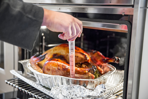 Delicious Thanksgiving turkey is being basted using a plastic baster by man. It is in a tin foil roasting pan. There is stuffing in the turkey and the pan and the giblets are in tin foil next to the pan. Close up shot taken with Canon 5D Mark 3.  rm