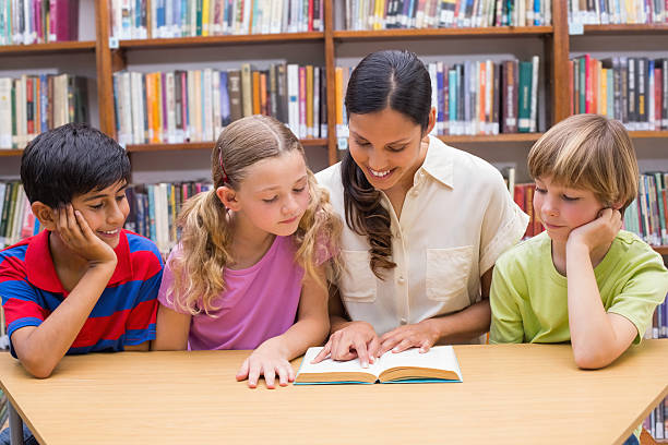 istock Cute pupils and teacher reading in library 473607788