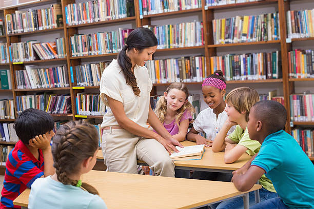 istock Cute pupils and teacher reading in library 473607794