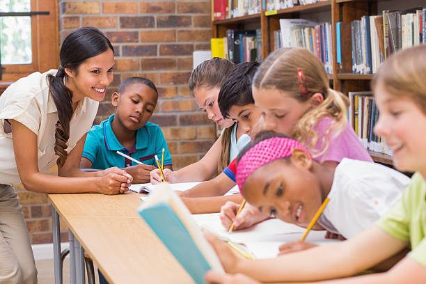 istock Pretty teacher helping pupils in library 473607824