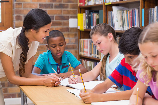 istock Pretty teacher helping pupils in library 473607828