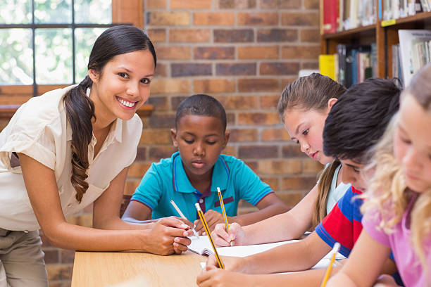istock Pretty teacher helping pupils in library 473607832
