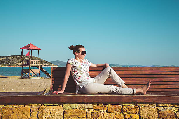 istock Young woman sitting on a bench and sun tanning 473609186