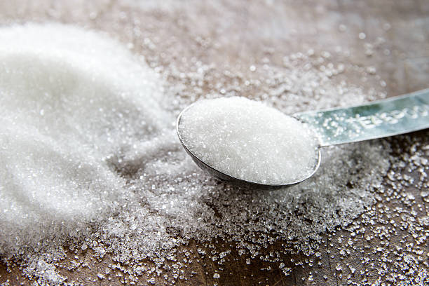 granulated sugar in spoon and sugar pile on wooden stock photo