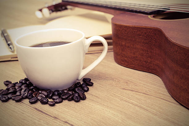Cup of coffee with ukulele and notebook on wooden table